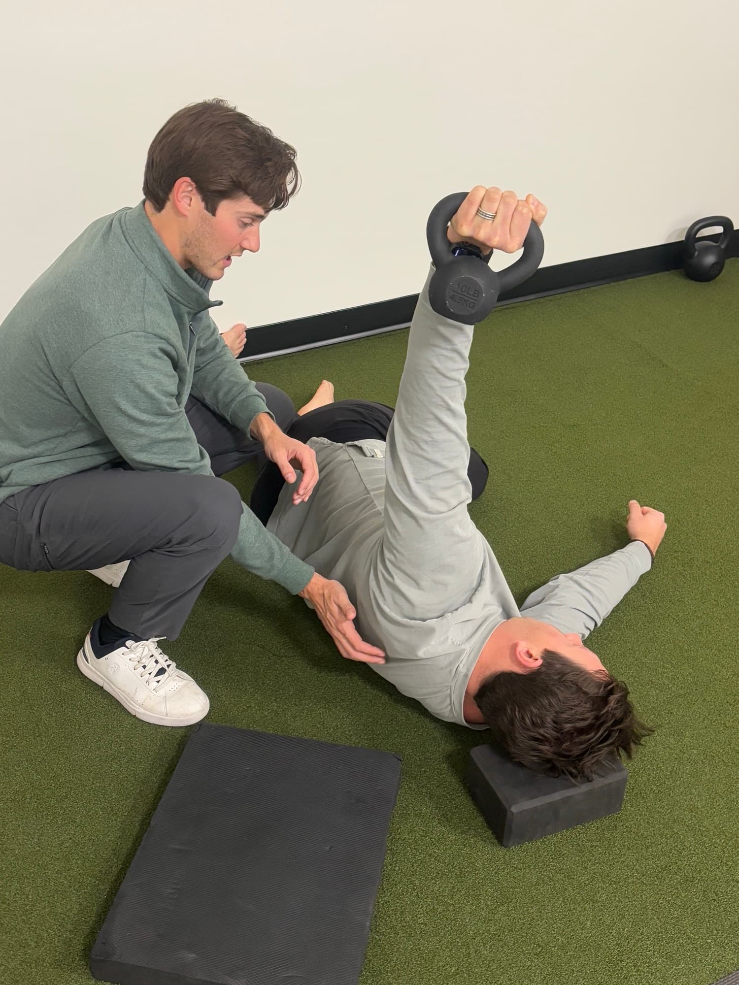 Dr. Taylor Wolf coaching a patient through a kettlebell floor exercise as part of a return-to-sport plan.
