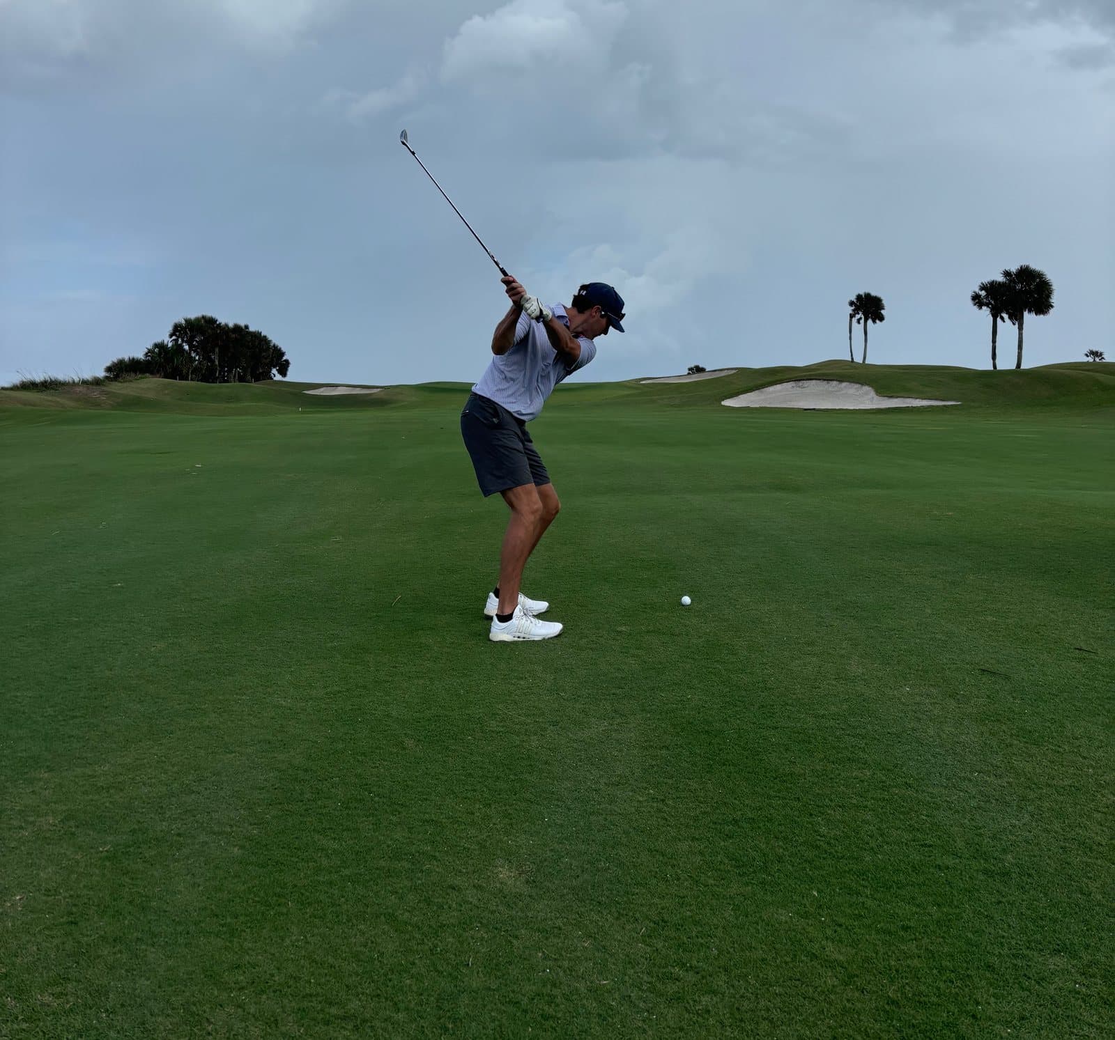 Golfer at the top of his swing on a fairway, the movement pattern golf performance chiropractic is built around.